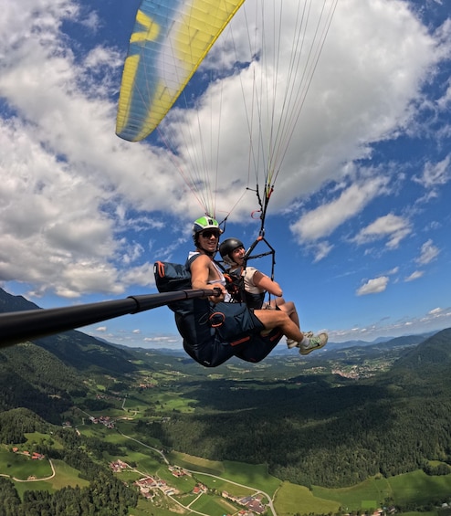A person paragliding over a mountainous landscape with visible roads and buildings below. 1