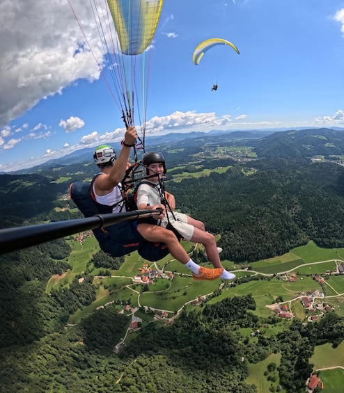 Two paragliders in mid-flight over a lush valley with a distant town. 3