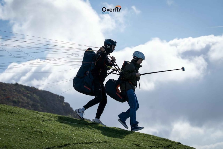 Two people with parachutes on a grassy hill with a cloudy sky. 4