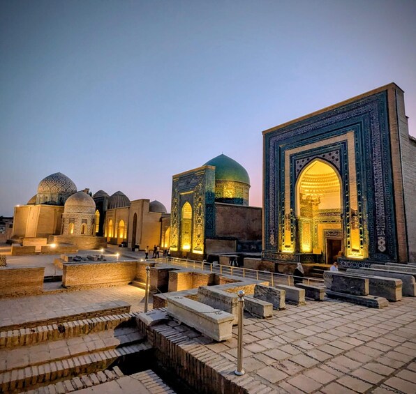 A historic building complex with domed structures and ornate architecture, illuminated at dusk. 1