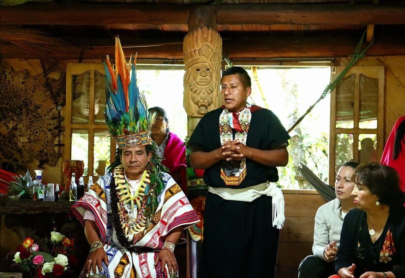 A traditional ceremony with participants in indigenous attire, a carved wooden totem, and a rustic interior. 4