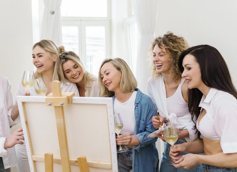 A group of people around an easel with a blank canvas, holding glasses of white wine. 3