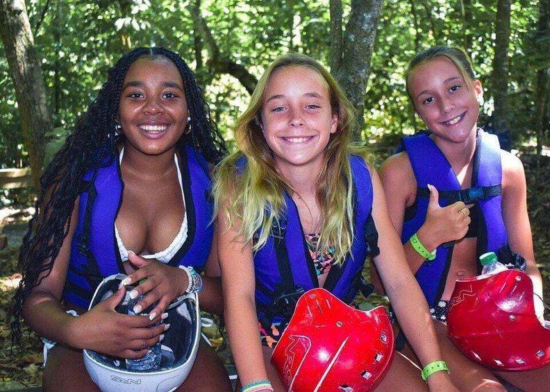 Three individuals in a forested area, each wearing a blue life jacket and holding a red helmet. 3