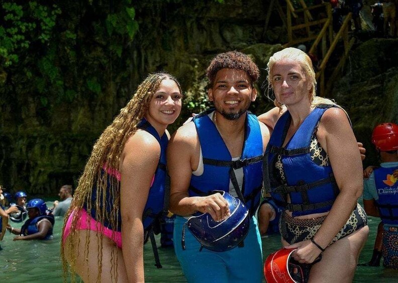 Three people wearing blue life vests, one holding a helmet, and a rocky background. 5