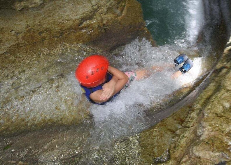 A person in a helmet and life jacket navigating through a narrow water channel between rocks. 4
