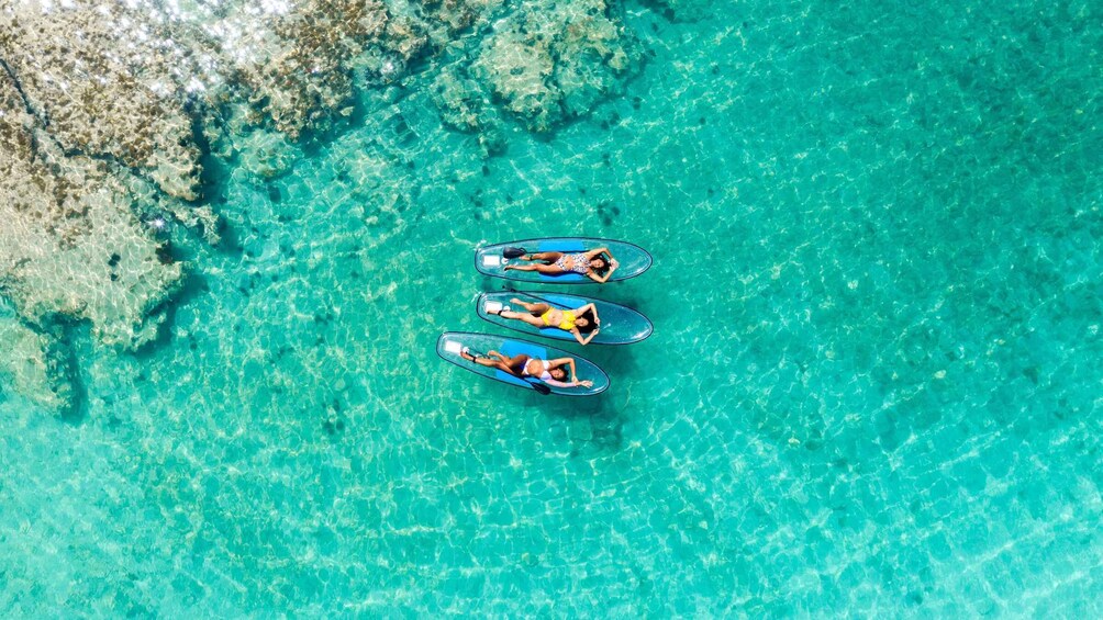 Three people on surfboards in clear turquoise water. 4