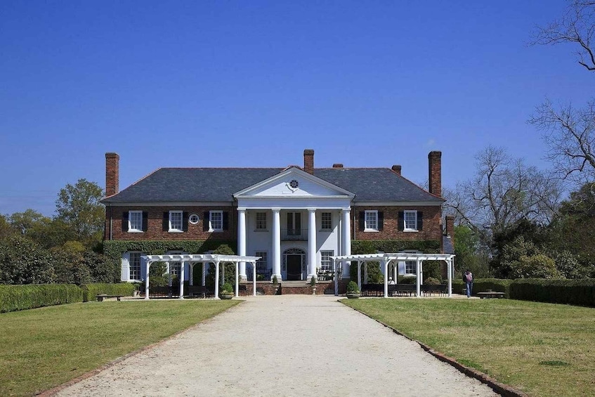 A large brick house with a central portico, surrounded by a well-maintained lawn and a gravel driveway. 2