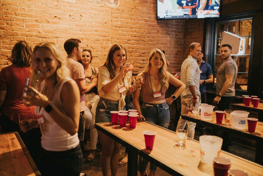 A group of people at a bar with red plastic cups and a television mounted on the wall. 3