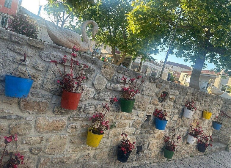 A stone wall with colorful hanging flower pots and a swan statue. 5