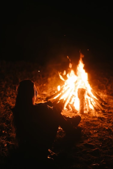 A person sitting by a campfire at night. 4