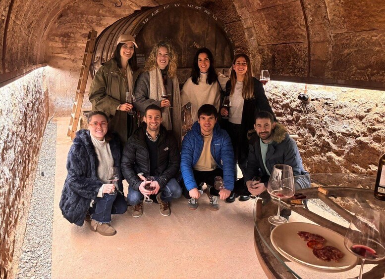 A group of people inside a cave with stone walls, holding glasses of wine, and a table with food and more wine. 1