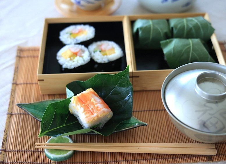 Sushi on a leaf, a bamboo mat, and a tea set. 1