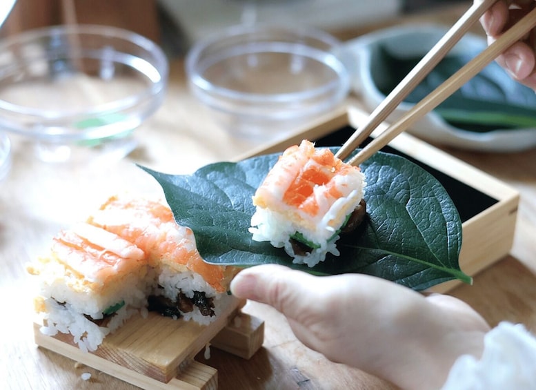 A sushi dish with salmon on a leaf, chopsticks, and a wooden board. 4