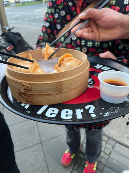 A person holding a bamboo steamer with dumplings and a dipping sauce. 2