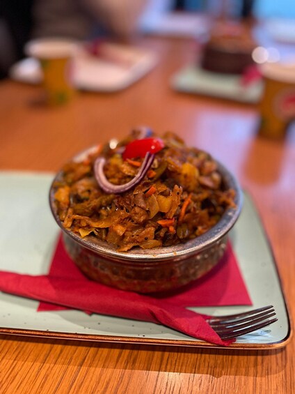 A bowl of food with a red garnish on a plate, placed on a table with a red napkin and a fork beside it. 3