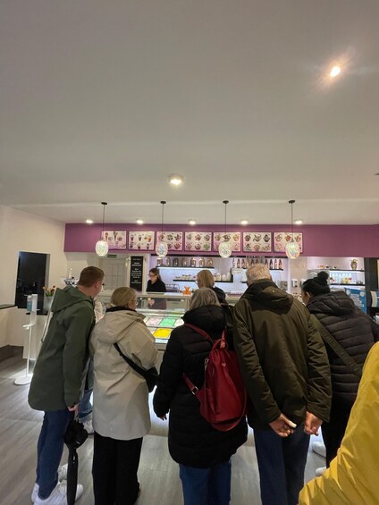 A group of people standing in line at a food counter with a menu above displaying various food items. 5