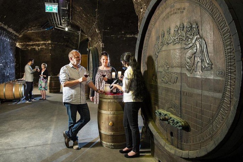 A group of people in a wine cellar with barrels and a large wine bottle. 3