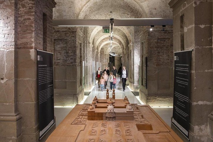 An indoor historical site with stone arches, a central display table, and informational signs. 2