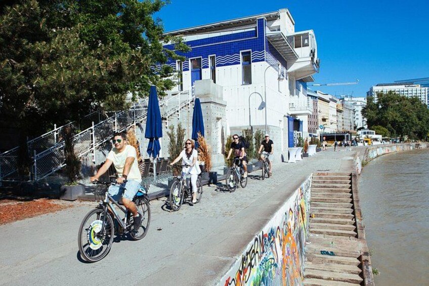 Una calle costera con ciclistas, un edificio azul y blanco, y un mural en la pared. 1
