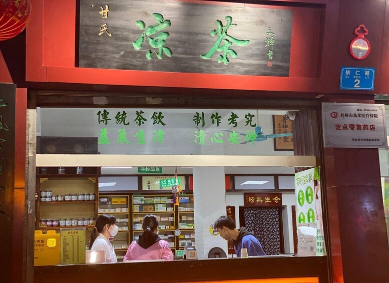 Ein traditioneller chinesischer Medizinladen mit einem Schild, Regalen voller Kräuterprodukte und einigen Kunden im Inneren. 5