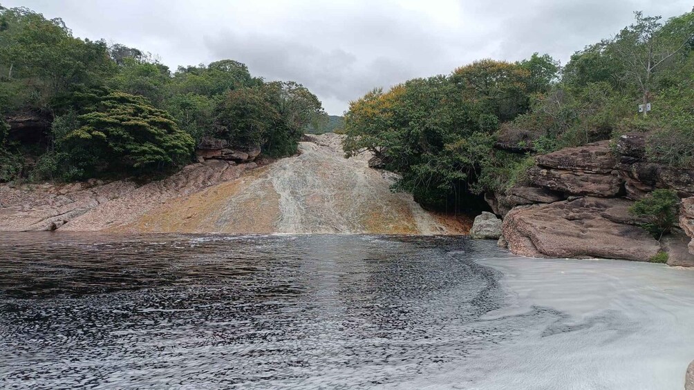 A river with rocky banks, dense foliage, and a cloudy sky. 1