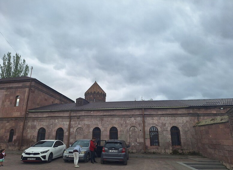 A historic building with a pointed tower, parked cars, and a cloudy sky. 4