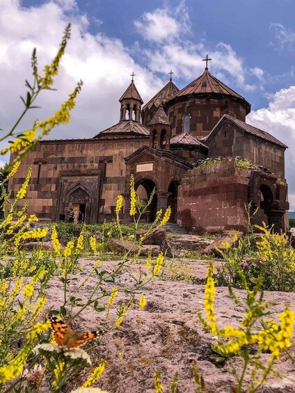 A historic church with multiple domes and crosses, surrounded by wildflowers and a butterfly. 1