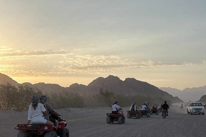 Un grupo de personas en cuatrimotos y un coche circulando por un camino de tierra con montañas al fondo. 5