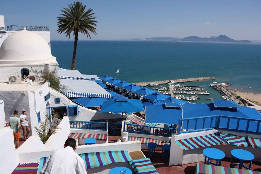 A seaside café with blue umbrellas and striped cushions overlooking a marina. 1