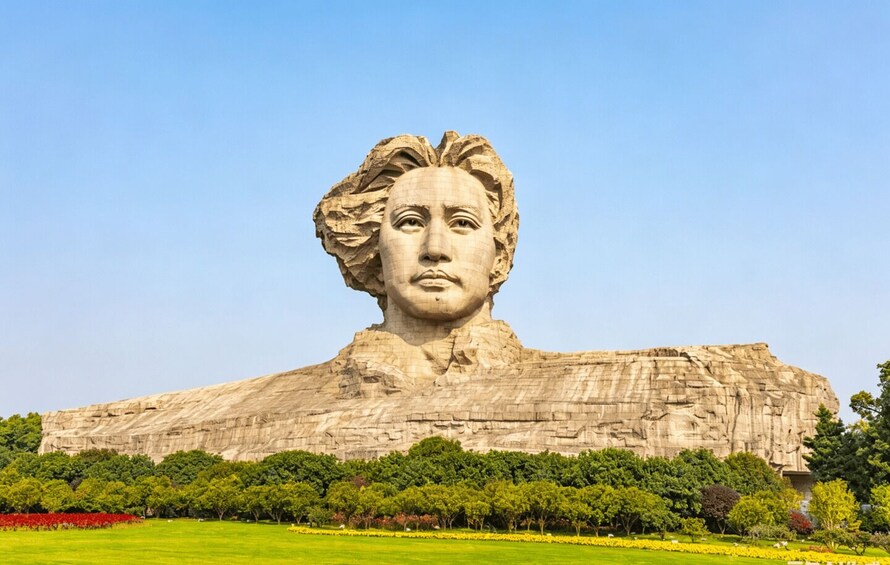 A large statue of a person with a blurred face, set against a clear blue sky, surrounded by a well-maintained park with green grass and trees. 5