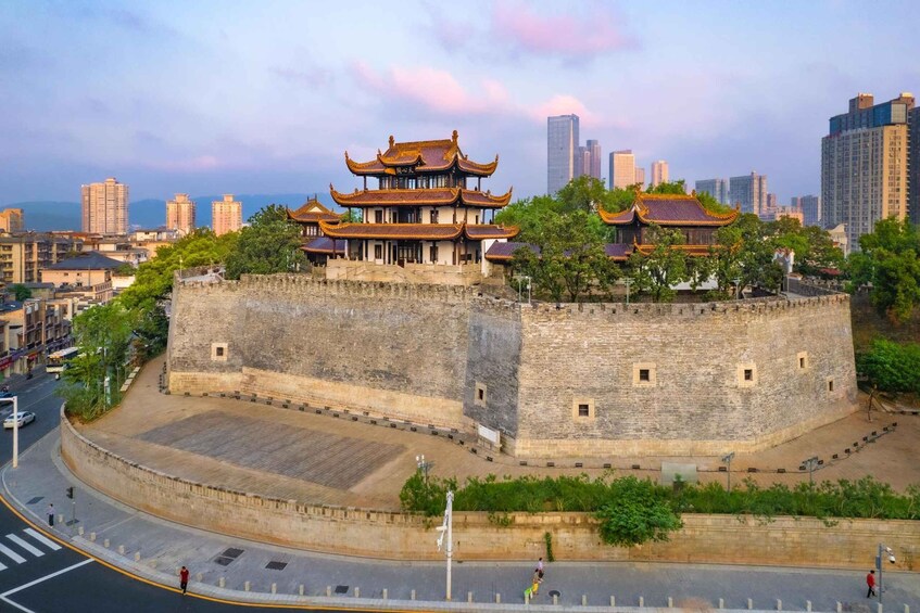 A traditional Chinese building with a multi-tiered roof, surrounded by a stone wall, set against a modern city skyline. 2