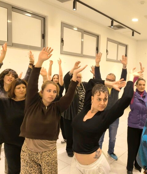 A group of people in a room with white walls and large windows, participating in a stretching or yoga session. 1