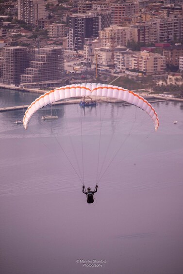 A paraglider descending towards a body of water with a cityscape in the background. 2