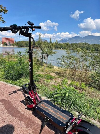 A stationary electric scooter parked on a path with a lake and mountains in the background. 3