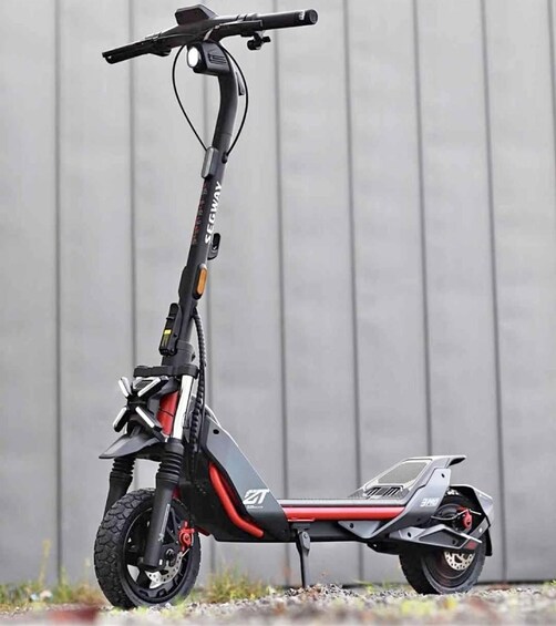 A Segway electric scooter with a black and red color scheme, a handlebar, and a kickstand. 2