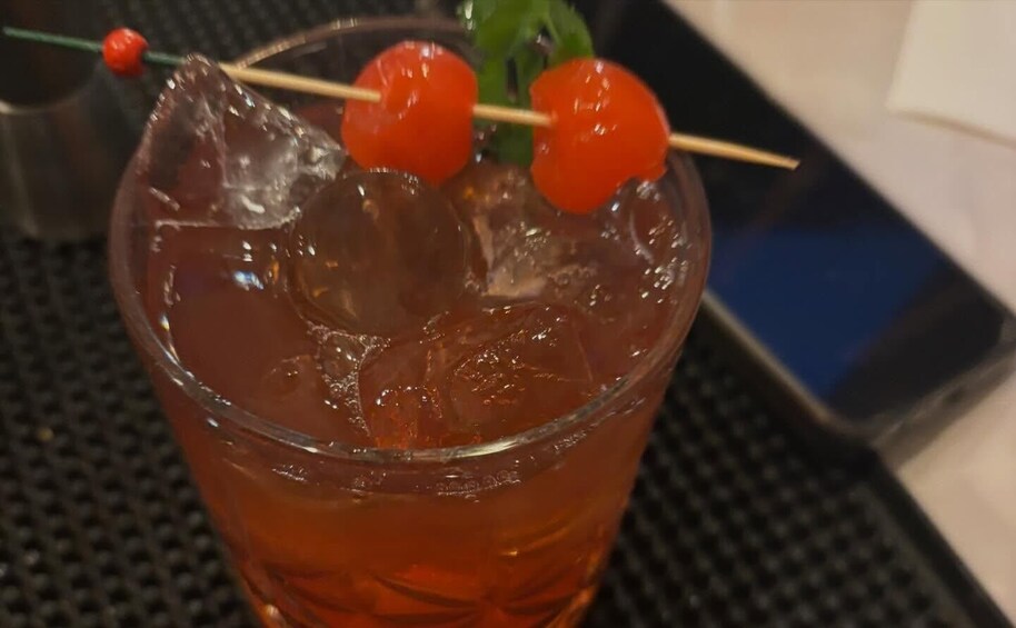 A glass with a dark amber liquid, ice cubes, and two cherry garnishes on a skewer. 5