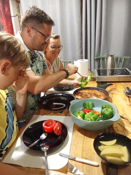 A family preparing food with bell peppers, tomatoes, and a frying pan on a wooden table. 1