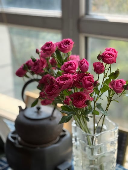 A vase with pink roses and a teapot on a windowsill. 5