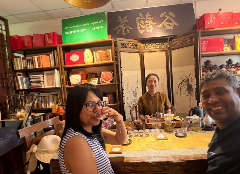 A tea shop interior with shelves of books and tea boxes, a tea tasting setup with cups and teapots, and traditional Chinese calligraphy on the wall. 4