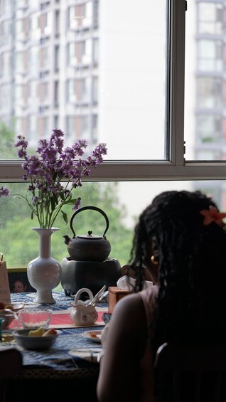A window with a view of a building, a vase with purple flowers, and a teapot on a table. 3