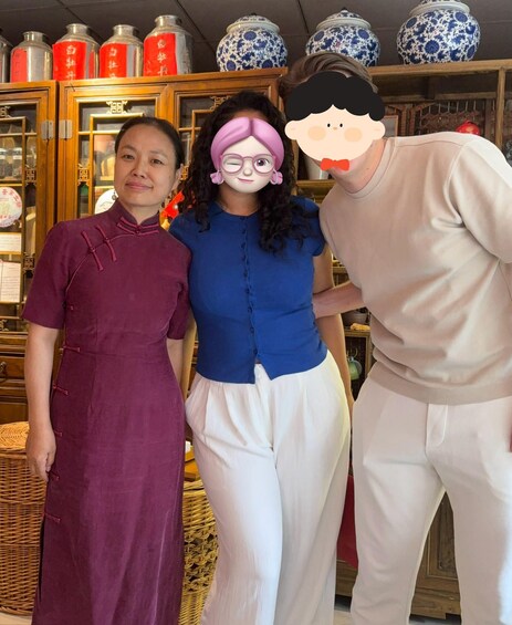 Three people in a room with traditional Chinese decor, including a cabinet with red and blue porcelain vases. 2