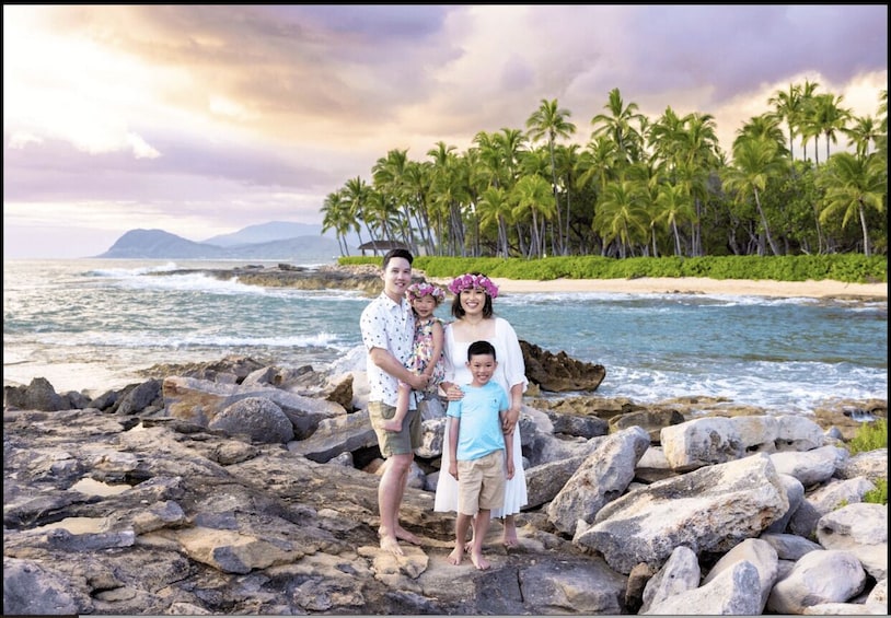 A family on a rocky beach with palm trees and ocean in the background. 1