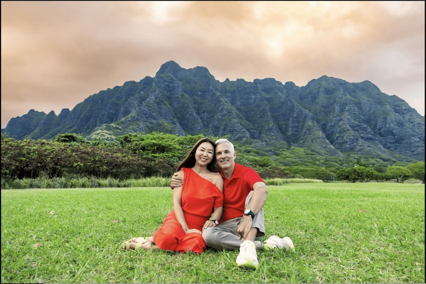 A couple sitting on grass with a mountain in the background. 2