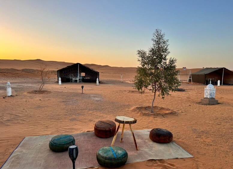 A desert landscape with a wooden structure, a tree, and traditional musical instruments on a mat. 1