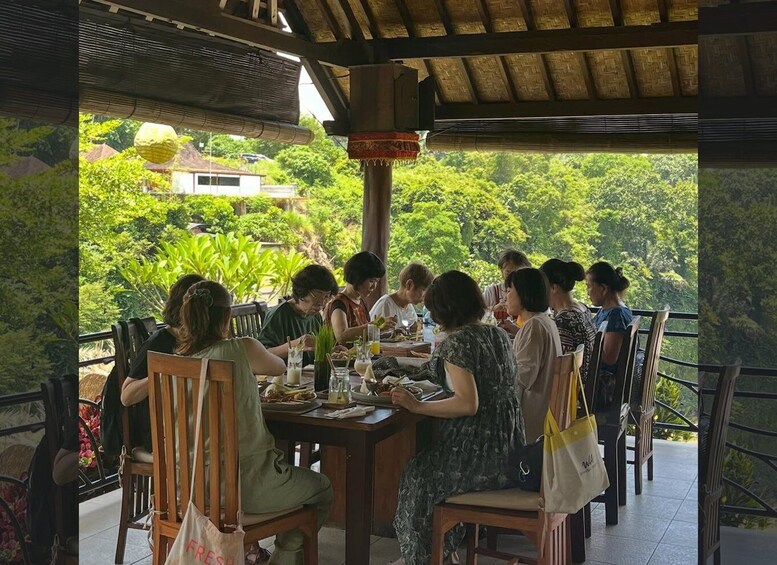 A group of people dining at an outdoor table with a view of lush greenery and a house in the background. 4