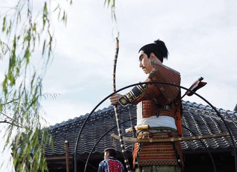 A person in traditional attire holding a long pole, standing on a structure with a tiled roof. 4