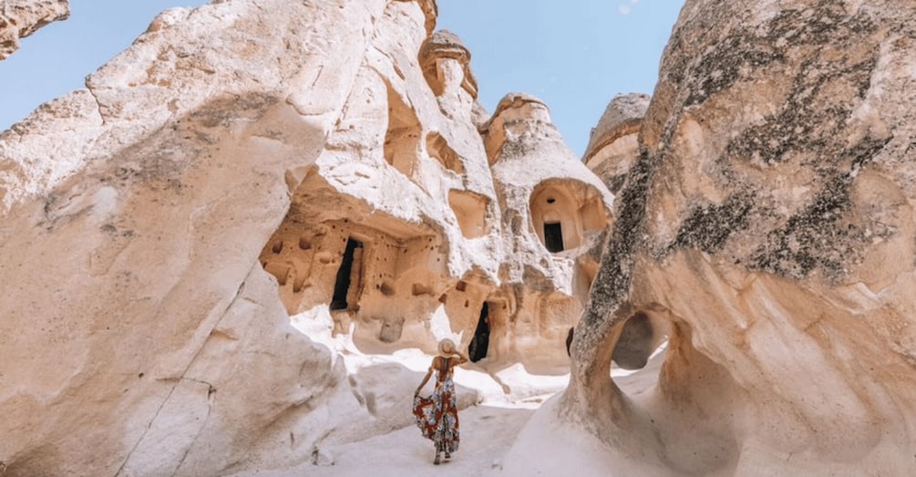 A person walking through a cave with multiple openings and a rocky landscape. 3