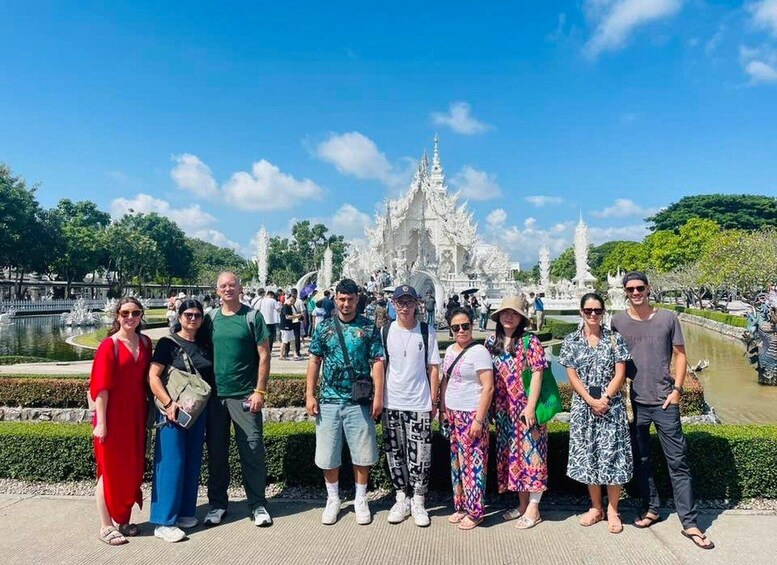 A group of people standing in front of a white, ornate structure with a fountain in the background. 3