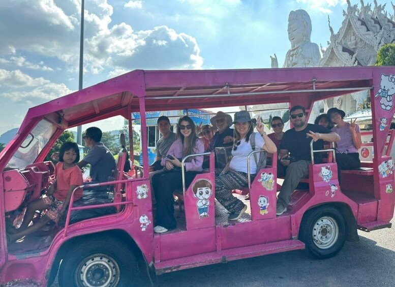 A pink vehicle with cartoon stickers, passengers, and a temple in the background. 4