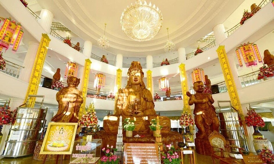 A multi-level shopping mall with large golden Buddha statues, chandeliers, and floral decorations. 5